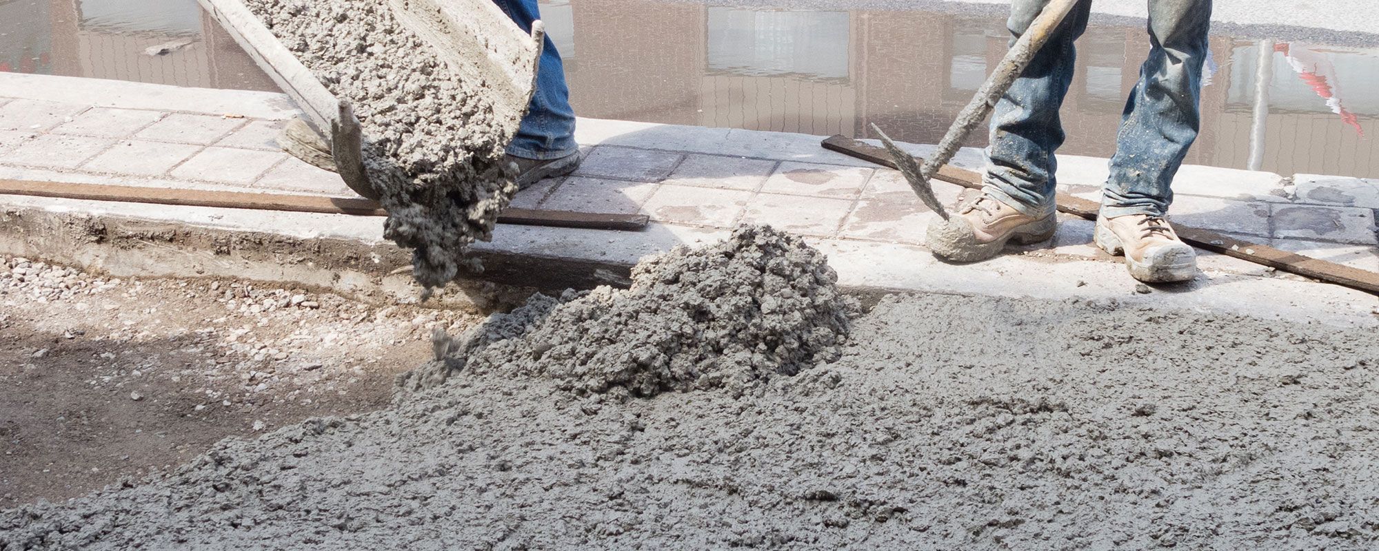 Zwei Bauarbeiter gießen nassen Beton aus einer Schubkarre auf ein Fundament