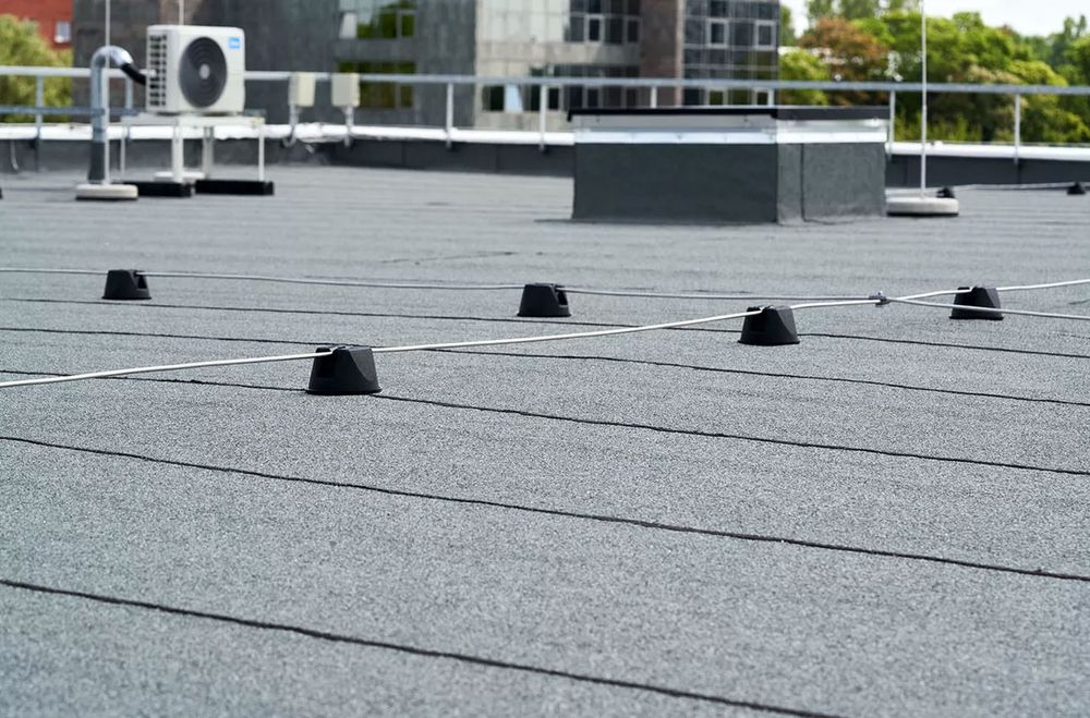 Ein mit grauem Filzmaterial bedecktes Flachdach mit schwarzen Stützblöcken